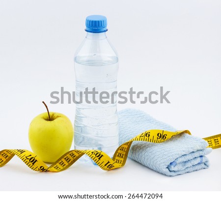 Healthy fitness concept. Bottle of water with apple, fitness towel and measuring tape on white background