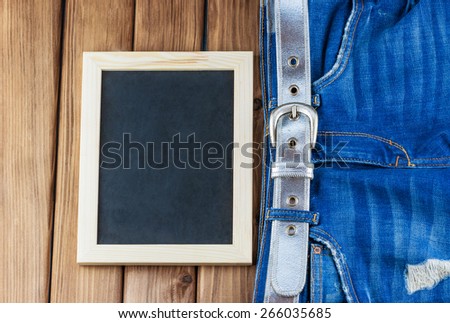 Top view of female jeans with belt and blank blackboard on wooden background