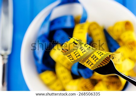 Healthy lifestyle concept. Close-up view of fork with measuring tape over the plate with knife on blue wooden background