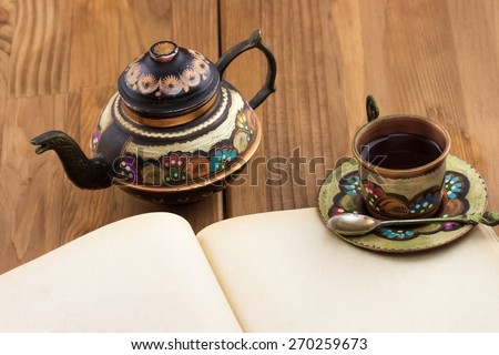 Top view of traditional Turkish copper teapot and cup of tea with blank old book on wooden table