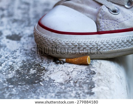 Shoes crushing a cigarette butt on asphalt