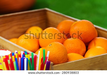 Heap of oranges in wooden box for orange juice with cups and tubes