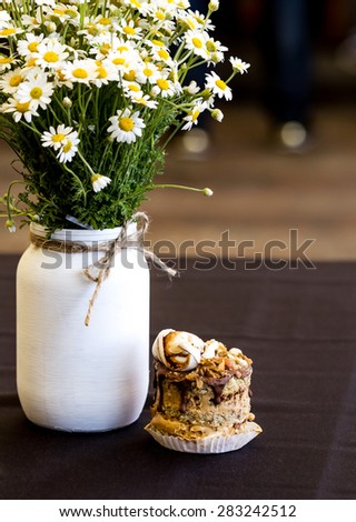 Vintage handmade vase with chamomile flowers and small cake on wooden table