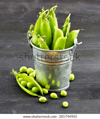 Close-up view of fresh green peas in a small metal bucket on dark wooden background