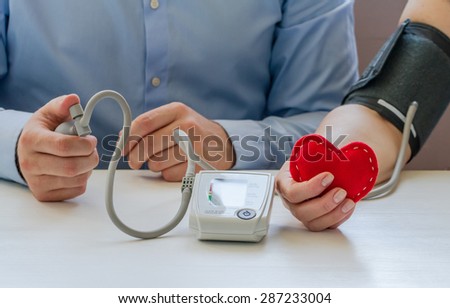 Doctor measuring blood pressure of senior woman taking red heart in the hand