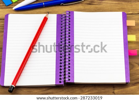Top view of notebook with red pencil and colorful stickers on wooden background
