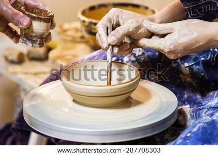 Female hand working on pottery wheel and draw a pattern on a clay plate