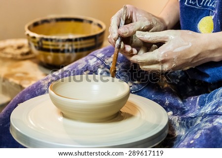 Female hand working on pottery wheel and draw a pattern on a clay plate