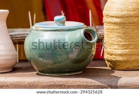 Close-up view of handmade green clay teapot on wooden shelf