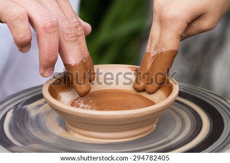 Woman with help of master hands working on pottery wheel and making clay plate