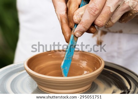 Master hand working on pottery wheel and draw a pattern on a clay plate