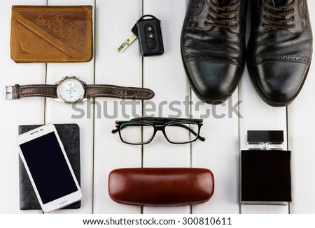 Top view of gentlemanly set: watches, auto document, car keys, shoes, glasses, smartphone, perfume on white wooden background