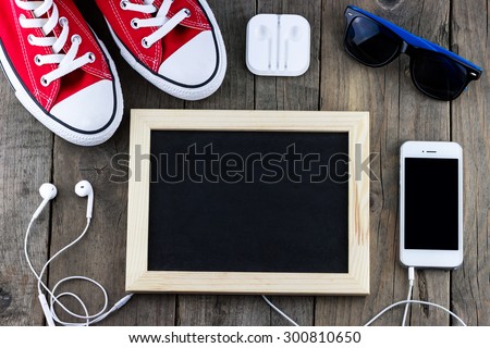 Top view of gentlemanly set: blank blackboard for text, red shoes, sunglasses, smartphone with headphones on old wooden background