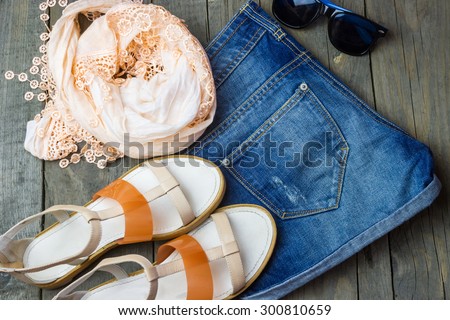 Top view of fashion women's set: sandals, denim shorts, blouse and sunglasses on old wooden background