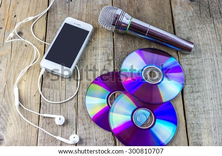 Top view of dvd disks, musical microphone, smartphone with headphones on old wooden background