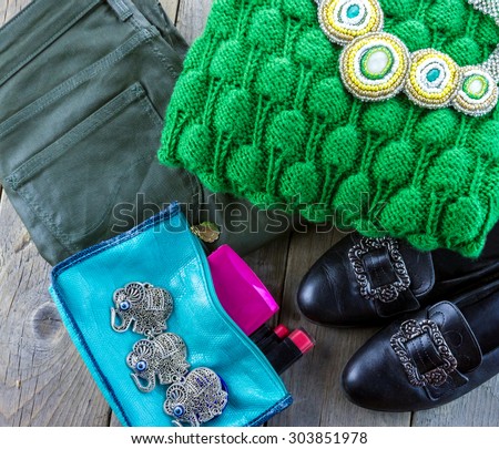 Top view of fashion women\'s set: retro shoes, green sweater, jeans, handmade necklace and cosmetics on wooden background