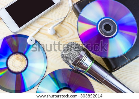 Top view of dvd disks, musical microphone, smartphone with headphones on wooden background