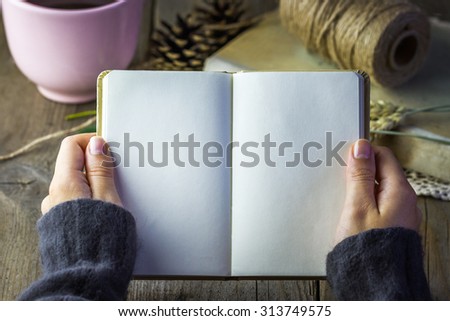 Autumn concept. Diary in female hands, with pink cup of hot tea, book, twine and cones