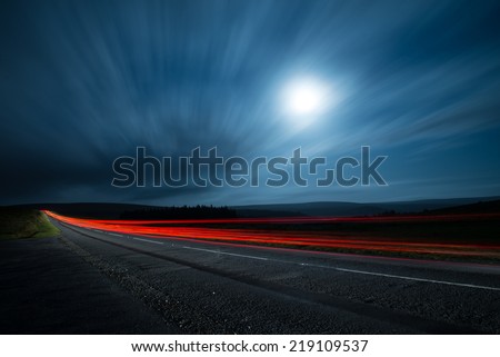 blur motion night shoot of fast driving car with clouds and moon
