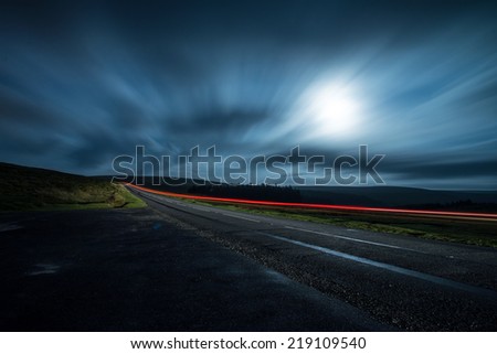 blur motion night shoot of fast driving car with clouds and moon