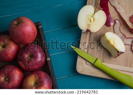 Fresh organic red apples on plate and apple halves on chopping wooden board and retro kitchen table in background