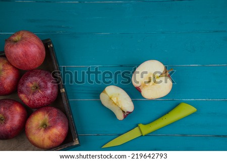 Fresh organic red apples on plate and apple halves on chopping wooden board and retro kitchen table in background