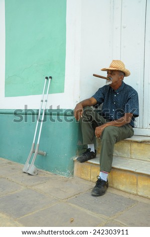 TRINIDAD, CUBA - MAY 26, 2013 Cuban local man smoking cigar and posing to photos while sitting on street in UNESCO protected city of Trinidad, Cuba.