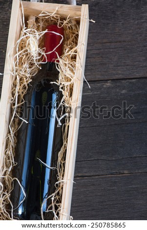 Red wine bottle in wooden case with straw on rustic background