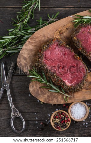 Raw peppered steak with herbs on wooden table