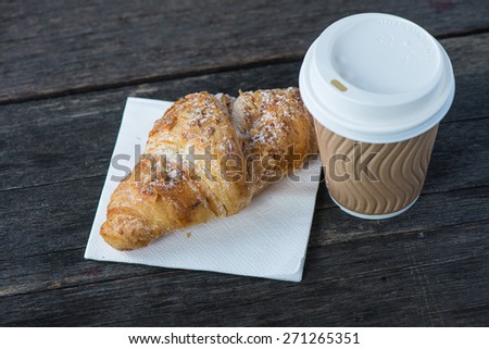 Take away coffee and fresh croissant on wooden background