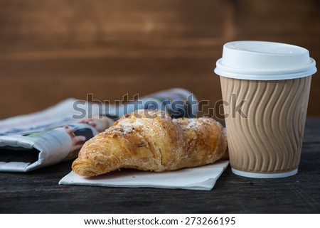 Take away coffee and fresh croissant and newspaper on wooden background