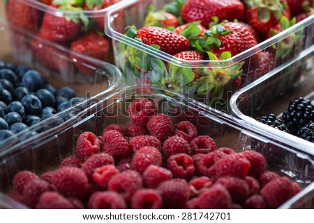 Farm fresh berries fruit in plastic trays on wooden table