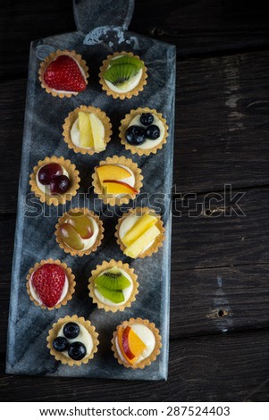 Mini pastry tartlets with fresh fruits, on marble serving board