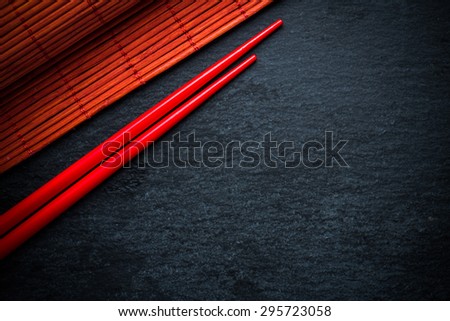 Japanese red chopsticks and bamboo mat on black slate, menu background