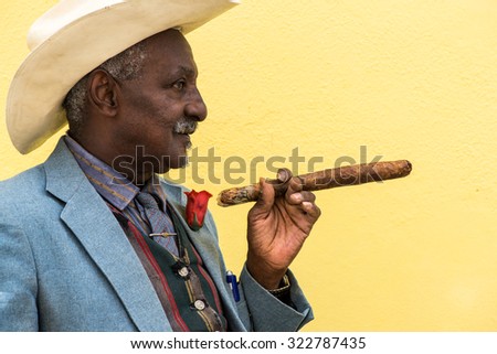 Havana, Cuba - September 27, 2015: Traditional Cuban man posing for photos while smoking big cuban cigar on yellow wall background in Havana, Cuba.