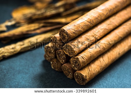 pile of authentic cuban cigars, tobacco leafs in background