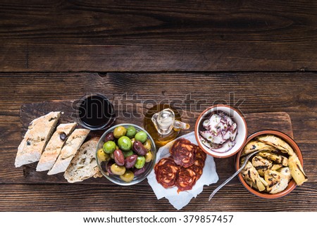 Wooden board with tapas, olives and salami and olive oil, from above, copy space for text or advert.