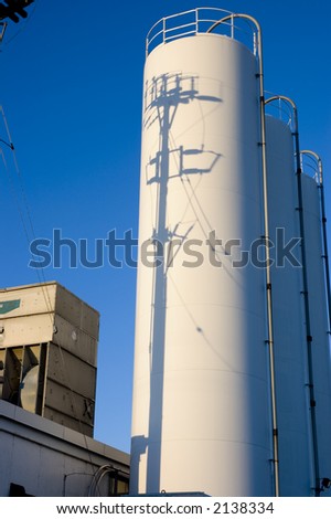 Industrial storage tanks outside of factory.  Shadow of hydro pole on tanks.