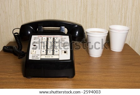 Telephone on night table in motel room.  Styrofoam coffee cups to the side.