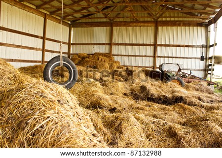 Old tire swing hanging above hay in a barn