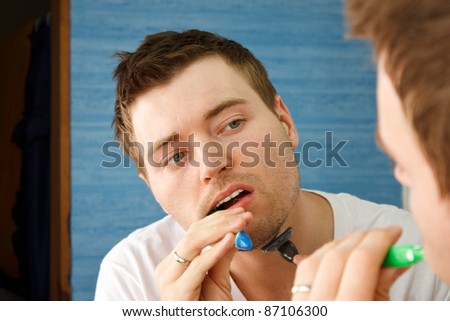 Young man multitasking by brushing teeth dry shaving at the same time