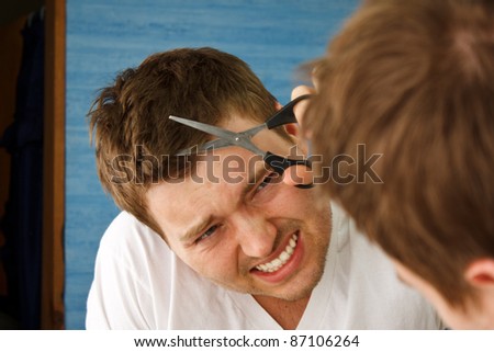 Young man preparing in mirror to cut hair himself with nervous expression