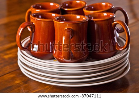 Six ceramic coffee cups sitting on a stack of dinner plates