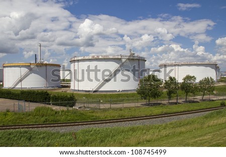 Three large white oil silos and a railway track belonging to an oil refinery in Rotterdam industrial area
