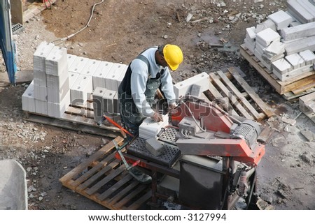 Black construction worker operating a brick-cutting machine at a construction site