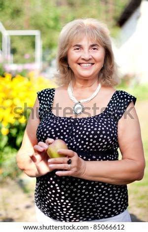 Beautiful mature woman open smiling with an apple in her hand outdoor
