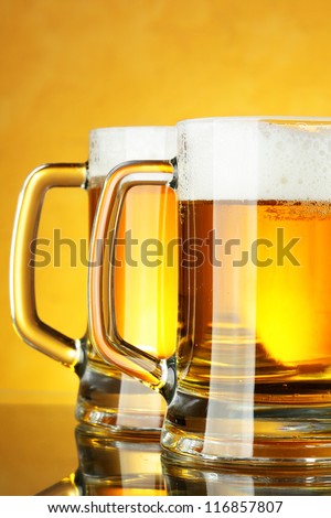 Beer mugs with froth over yellow background