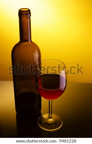 Still-life with glass and bottle of red wine over yellow background