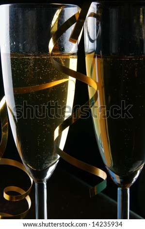 Two glasses of champagne and gold streamer over black background