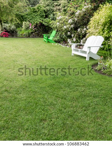 A beautiful green lawn surrounded by flowers with wooden lawn chairs